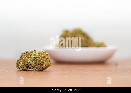 Eine kleine Cannabisknospe auf einem Tisch mit einer verschwommenen Schüssel im Hintergrund. Stockfoto