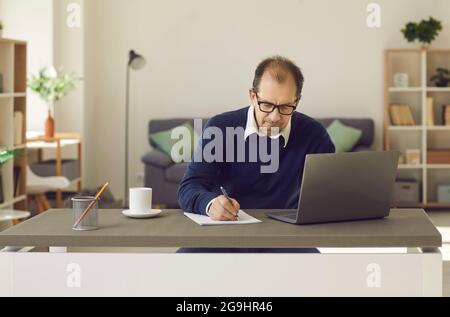 Reifer Mann sitzt vor dem Laptop-Bildschirm Schreiben auf Papier Notebook Porträt Stockfoto