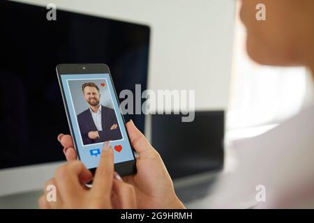 Frau mit Mobiltelefon und Blick auf das Bild des jungen Mannes auf der Online-Dating-App Stockfoto