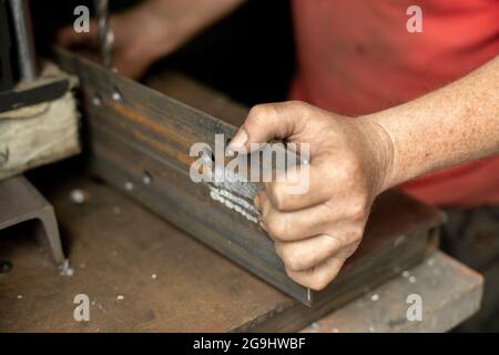 Gebohrte Löcher in das Metall. Arbeiten Sie in einer Metallwerkstatt. Die Hand hält einen Stahlrohling. Ein Mann arbeitet in der Garage. Stockfoto