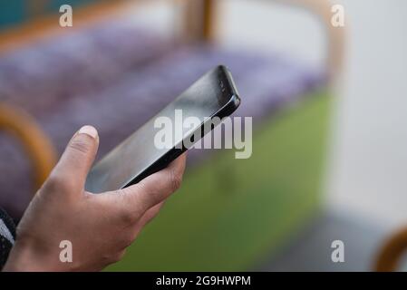 Shallow-Focus-Aufnahme der rechten Hand eines Mannes, der ein schwarzes Smartphone in einem Bus hält Stockfoto