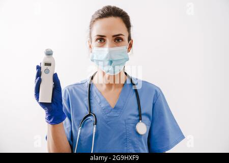 Junge schöne selbstbewusste Frau Arzt trägt Stethoskop zeigt Thermometer isoliert auf weißem Hintergrund Stockfoto
