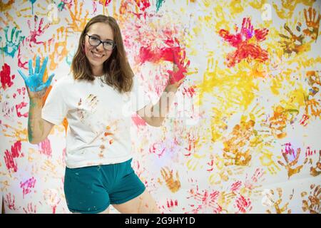 Portrait einer netten glücklichen Frau malen und Spaß haben. Sie zeigt ihre Hände Gesicht und Kleider in hellen Farben gemalt Stockfoto