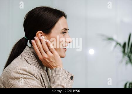 Glückliche Erwachsene Frau, die mit Ohrhörern Musik hört und im Büro lächelt Stockfoto