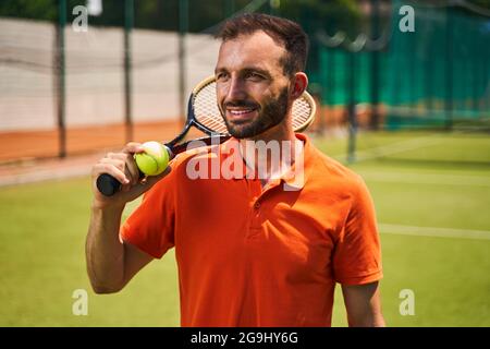 Fröhlicher männlicher Spieler, der auf dem Tennisplatz steht Stockfoto
