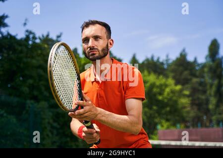 Ernsthaft fokussierter junger Mann, der im Freien Tennis spielt Stockfoto