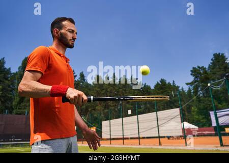 Fokussierter, dunkelhaariger Sportler, der einen Ball auf dem Schläger hüpft Stockfoto