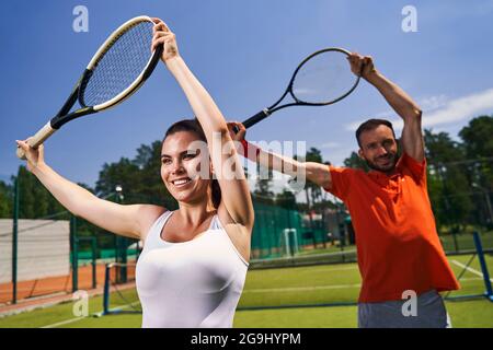 Zwei Tennisspieler strecken ihre Armmuskeln mit ihren Schlägern Stockfoto