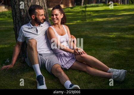 Romantisches Paar, das unter einem Baum in einem Park sitzt Stockfoto