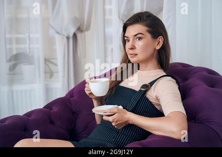 Nette junge Frau genießt ihren Kaffee im Salon Stockfoto