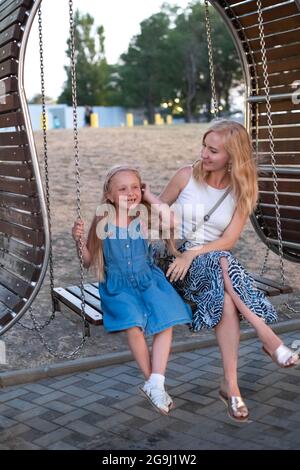 Junge Mutter und Tochter auf Schaukel. Sommerurlaub. Das Konzept der Kindererziehung. Stockfoto