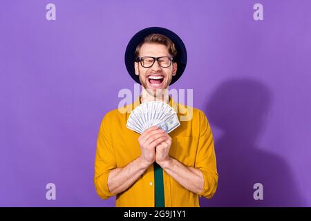 Foto von jungen aufgeregt Kerl glücklich positive Lächeln reichen Dollar Banknoten Einkommen isoliert über lila Farbe Hintergrund Stockfoto