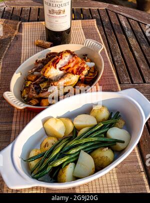 Abendessen im Freien: Gebratener Faasan mit Gemüse und Pancetta, neue Kartoffeln und grüne Bohnen, eine Flasche französischer Saint Emilion Rotwein Stockfoto