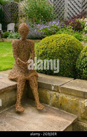 Weidenskulptur Kunst des Mädchens (ornamentales Merkmal) in einem wunderschönen Landschaftsgarten (blühende Stauden, Kastenbälle, Rasen, ) - Yorkshire, England, VEREINIGTES KÖNIGREICH. Stockfoto