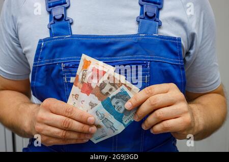 Ein kolumbianischer Arbeiter hält Geld in der Hand, EIN paar Pesos-Banknoten in kleinen Stückelungen, das Konzept der Löhne für Berufstätige und Arbeiter Stockfoto