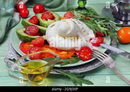 Burrata mit Tomaten, Rucola, Avocado und Wein auf grünem Hintergrund Stockfoto