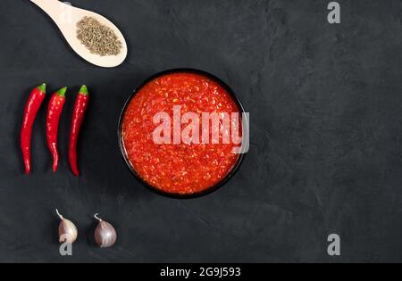 Harissa Sauce auf schwarzem Hintergrund. Adjika-Sauce mit scharfer Chilischote. Blick von oben. Platz für Text. Stockfoto
