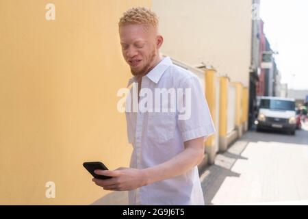 Deutschland, Köln, Albino Mann in weißem Hemd mit Smartphone Stockfoto