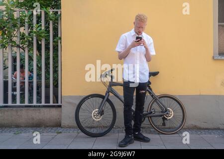 Deutschland, Köln, Albino Mann mit Smartphone vor dem Gebäude und Fahrrad Stockfoto