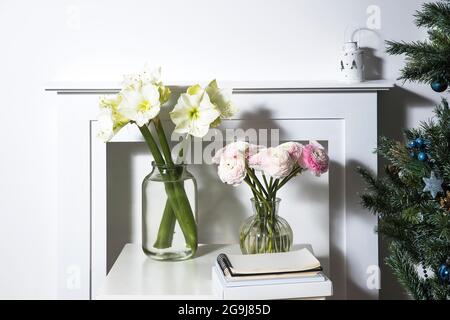 Ein Bouquet von rosa persischen Butterblumen in einer Glasvase und zwei eingewickelte Geschenke auf einem weißen Tisch vor einem falschen weißen Kamin. Bouquet von weißem amary Stockfoto