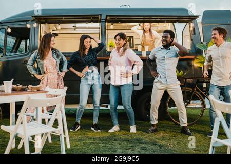 Multirassische Freunde tanzen in der Nähe von Food Truck im Park Stockfoto