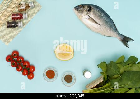 Flach legen frisch rohes dorado mit Tomaten, Zitronen, Spinat und Gewürzen auf Blau Stockfoto