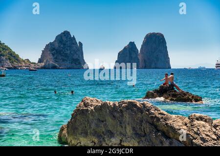CAPRI, ITALIEN - 15. JUNI 2021: Touristen besuchen den Strand Marina Piccola mit Blick auf den berühmten Faraglioni Stockfoto