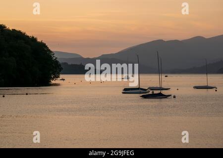 Boote auf dem Lake Windermere, wenn die Sonne hinter den Bergen untergeht. Stockfoto