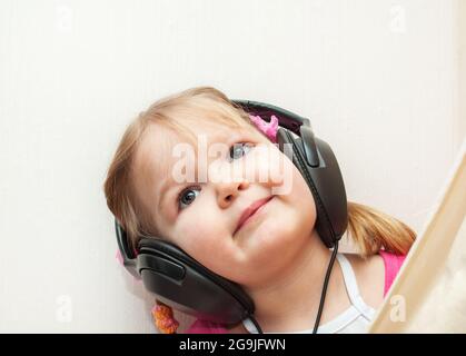 Niedliches Baby mit Kopfhörern, die die Kamera betrachten. Kleines schönes Mädchen in Kopfhörern hört Musik Stockfoto