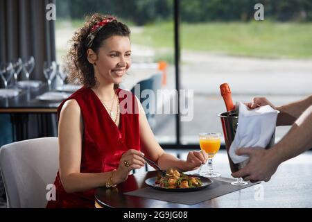 Der Kellner brachte einer jungen Frau im Restaurant Champagner im Eimer mit Eis Stockfoto