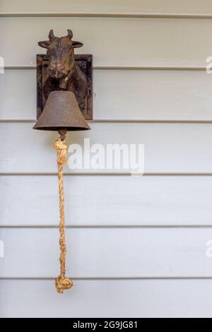 Eine gusseiserne Kuhtür hängt an einer ländlichen Wetterschutzhütte an der Hintertür, um die Familie zum Essen, Telefonieren usw. zu rufen Stockfoto