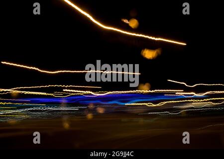 Fahren In Der Stadt. Leichter Regen. Langzeitbelichtung. Blick durch die Windschutzscheibe während der Nachtfahrt. Langzeitbelichtung. Künstlerisch, abstrakt. Stockfoto