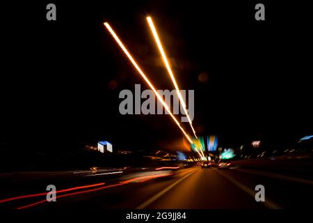 Fahren In Der Stadt. Leichter Regen. Langzeitbelichtung. Blick durch die Windschutzscheibe während der Nachtfahrt. Langzeitbelichtung. Künstlerisch, abstrakt. Stockfoto