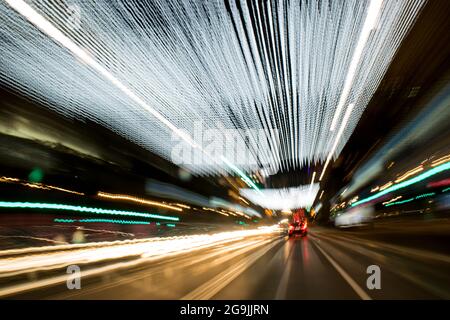 Fahren In Der Stadt. Leichter Regen. Langzeitbelichtung. Blick durch die Windschutzscheibe während der Nachtfahrt. Langzeitbelichtung. Künstlerisch, abstrakt. Stockfoto