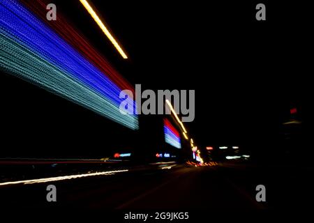 Fahren In Der Stadt. Leichter Regen. Langzeitbelichtung. Blick durch die Windschutzscheibe während der Nachtfahrt. Langzeitbelichtung. Künstlerisch, abstrakt. Stockfoto