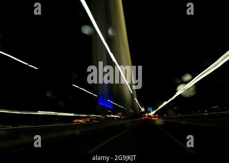 Fahren In Der Stadt. Leichter Regen. Langzeitbelichtung. Blick durch die Windschutzscheibe während der Nachtfahrt. Langzeitbelichtung. Künstlerisch, abstrakt. Stockfoto