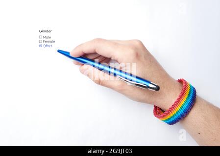 Hand der nicht erkennbaren Person schriftlich und Kennzeichnung der handschriftlichen Option andere in einer Form, um das Geschlecht zu wählen, trägt ein Armband mit dem Regenbogen Fla Stockfoto