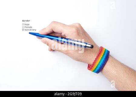 Hand einer nicht erkennbaren Person, die die nicht-binäre Option auf einem Formular markiert, das diese Option zur Geschlechtsidentität enthält, und ein Armband mit dem Regenbogen f trägt Stockfoto