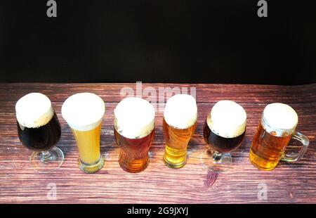 Auf einem Holztisch stehen sechs Gläser verschiedener Biersorten in einer Reihe. Blick von oben. Stockfoto