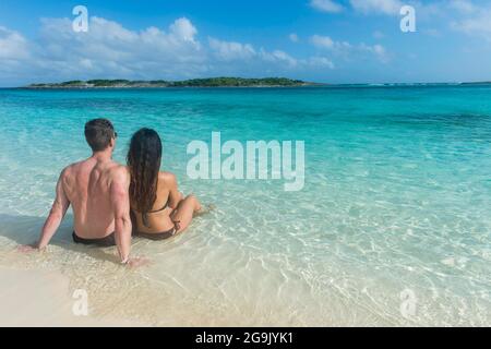 Pärchen, die an einem weißen Sandstrand im türkisfarbenen Wasser der Exumas, Bahamas, Karibik, sitzen Stockfoto