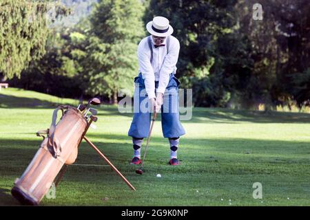 Ein älterer Mann mit Strohhut und Knickerbockern, die auf einem Golfplatz Hickory Golf spielen Stockfoto