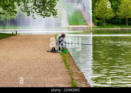 Älterer brauner Mann, der in einem See mit formellen Gärten in Sceaux, Frankreich, fischt Stockfoto