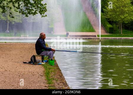 Älterer brauner Mann, der in einem See mit formellen Gärten in Sceaux, Frankreich, fischt Stockfoto