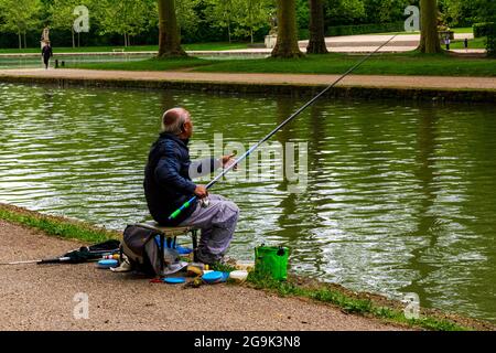 Älterer brauner Mann, der in einem See mit formellen Gärten in Sceaux, Frankreich, fischt Stockfoto