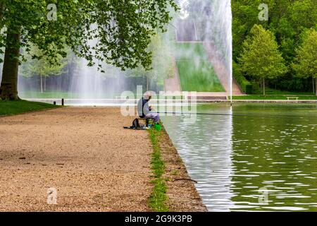 Älterer brauner Mann, der in einem See mit formellen Gärten in Sceaux, Frankreich, fischt Stockfoto