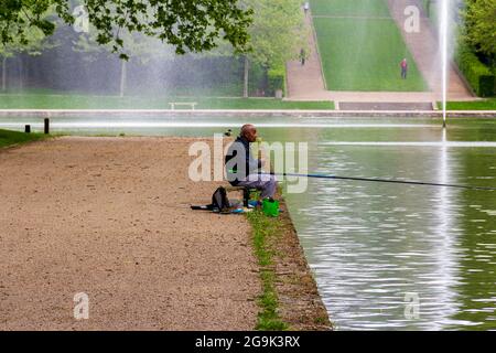 Älterer brauner Mann, der in einem See mit formellen Gärten in Sceaux, Frankreich, fischt Stockfoto