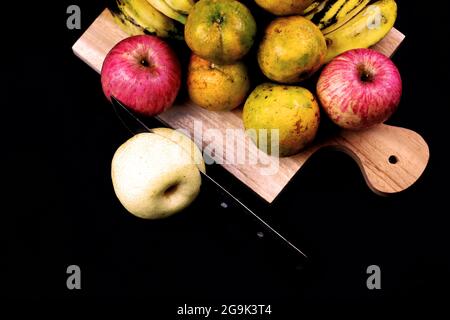 Foto von flach ausgeschnitter Birne und einigen Orangen, Äpfeln, Bananen auf schwarzem Hintergrund Stockfoto