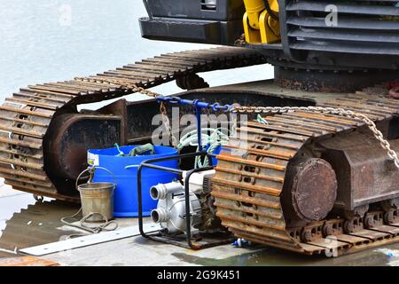 Detail der Spuren eines schweren Raupenfahrzeugs mit Wasseroberfläche im Hintergrund. Stockfoto