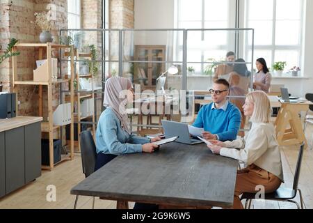 Muslimische junge Bewerberin sitzt am Tisch vor zwei Arbeitgebern Stockfoto