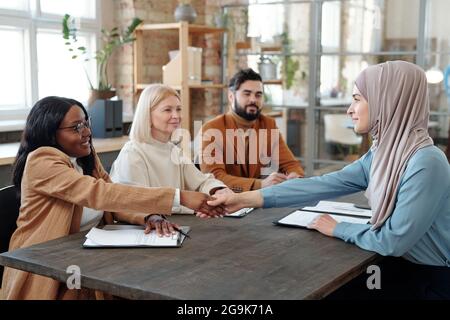 Glückliche afrikanische Geschäftsfrau schüttelt nach dem Interview die Hand der muslimischen Bewerberin Stockfoto